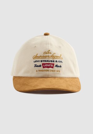 Boné de basebol creme com aba de camurça castanha e texto bordado incluindo "Levi's" e "Uma Tradição Desde 1873" no painel frontal.
