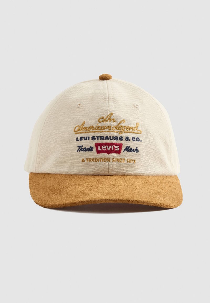 Cream baseball cap with tan suede brim and embroidered text including "Levi's" and "A Tradition Since 1873" on front panel.