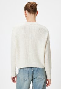 Maglione crema a coste con maniche lunghe, orlo leggermente corto e lavorazione a maglia testurizzata. Abbinato a jeans chiari a vita alta.