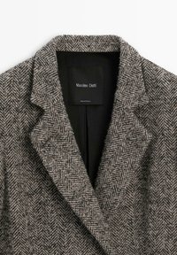 Cappotto in misto lana grigio e marrone con motivo a spina di pesce. Collo a scatto, foderato internamente in nero, con un'etichetta con il marchio "Massimo Dutti".