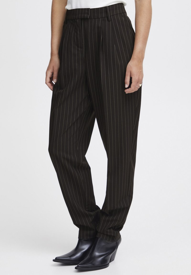 Zwarte pinstripe broeken met een hoge taille, taps toelopende benen en voorplooien. Gecombineerd met zwarte leren enkellaarsjes met hak.