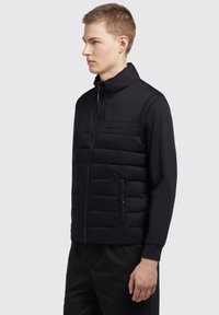Sort, polstret veste med høj krave og frontlynlås. Har to sidelommer, tekstureret stof og minimal branding på brystet.