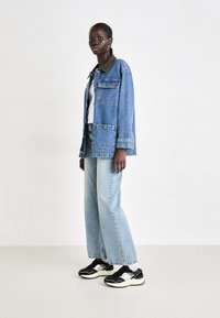 Chaqueta de mezclilla con dos bolsillos frontales, lavado azul claro, corte oversize, combinada con jeans azul claro y zapatillas negras con detalles blancos.