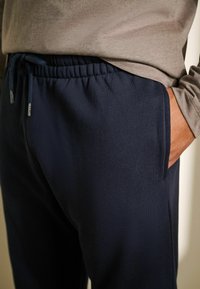 Pantaloni da jogging blu navy con cintura elastica e coulisse, dotati di tasche laterali e una finitura in tessuto morbido e strutturato.