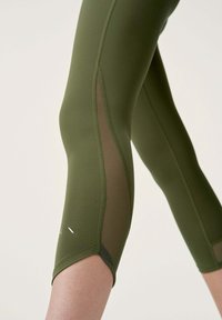 Olivgrüne Leggings mit Netz-Seitenpaneelen, figurnaher Passform und glatter Textur. Enthält ein weißes Logo-Detail nahe dem Saum.