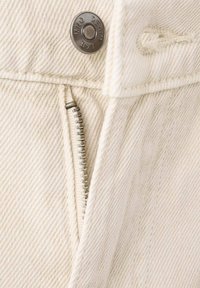 Biele rifle z denimu so strieborným zipsom a zapínaním na gombík, s textúrovanou látkou a čistými líniami, zdôrazňujúce detail zipsu.