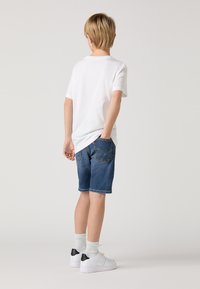 Short denim shorts with a classic blue wash, a straight cut, front and back pockets, worn with a white t-shirt and white sneakers.