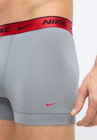 Sivé bavlnené boxerky majú na páse červené logo Nike a malé červené logo swoosh na boku. Hladká textúra, priliehavý dizajn.