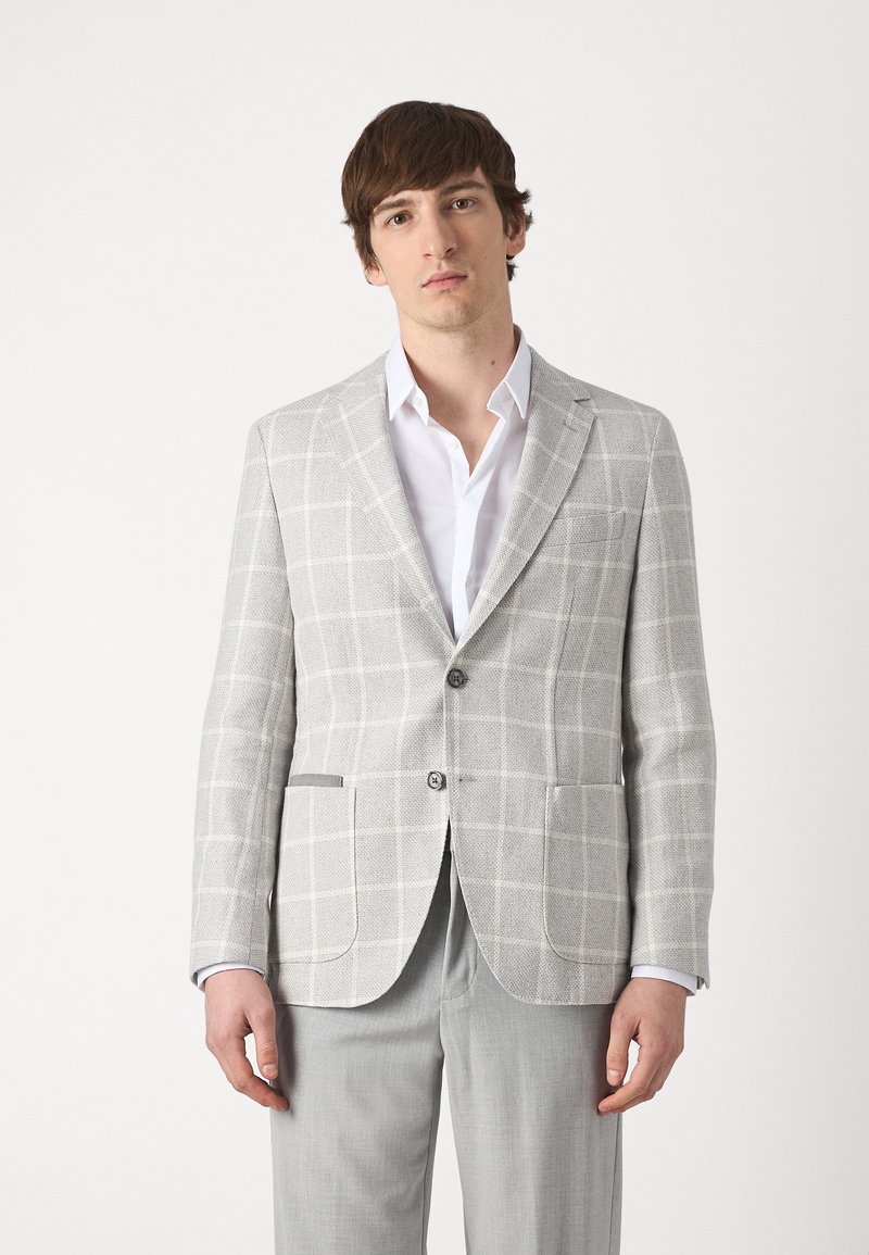 Lichtgrijze blazer met een geruit patroon, twee knopen en opgestikte zakken. Gecombineerd met een wit overhemd en grijze broek.