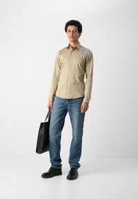 Beige gombos ing, kék farmernadrág, fekete bőrcipők és egy fekete táska. Simaszövet és klasszikus szabás. Egyszerű dizájnelemek.