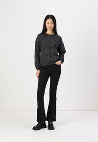 Felpa nera con design grafico del volto di una donna e testo. Abbinata a jeans neri a zampa d'elefante e stivali neri con tacco platform. Estetica semplice e moderna.