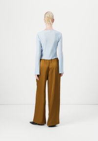 Svetlomodrý rebrovaný dlhý rukáv s okrúhlym výstrihom v kombinácii so širokými hnedými nohavicami. Čierna obuv dotvára celkový outfit.