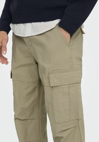 Kevyet khakinväriset cargohousut, joissa on useita sivutaskuja, kevyt kangas hienovaraisella tekstuurilla ja rento istuvuus.