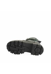 Black footwear with a rugged rubber sole featuring a zigzag tread pattern. Metallic chain accenting at the top, overall sturdy design.