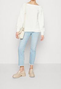 Maglione bianco lavorato a maglia, jeans cropped azzurri leggeri e mocassini beige con tacco spesso. Piccola borsa a tracolla con catena e dettagli in oro.