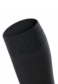Calza nera in maglia con una texture a coste, caratterizzata da un ampio risvolto superiore e un corpo liscio che si trasforma in una forma affusolata.