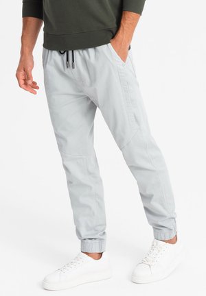Hellgraue Jogginghose aus weichem Stoff, mit elastischem Bund, seitlichen Taschen und gerippten Säumen. Kombiniert mit weißen Sneakers.
