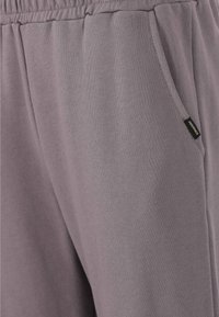 Grå mjukisbyxor med elastisk midja, sidofickor och en liten etikettaccent vid höften, som visar ett mjukt, texturerat tyg.