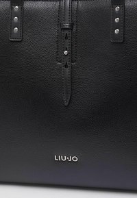 Sac à main en cuir noir à surface texturée, avec des accents en métal argenté et le logo "LIU•JO" embossé en bas.