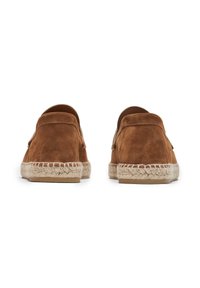 Zapatos de ante marrón tipo mocasín con suela de cuerda natural y tacón plano. Presentan un respaldo redondeado y detalles de costura a lo largo del borde de la suela.