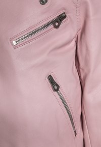 Světle růžová kožená bunda s dvěma zipovými kapsami a stříbrnými detaily. Textura je hladká s viditelnými švy.