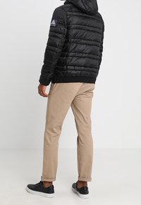 Czarna kurtka puchowa z kapturem, z prostokątnym pikowanym wzorem i logo na ramieniu. Połączona z beżowymi spodniami i czarnymi trampkami.