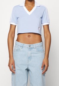 Polo shirt cropped di colore azzurro con colletto e polsini bianchi. Caratterizzato da uno scollo a V, maniche corte e dettagli in ricamo floreale.