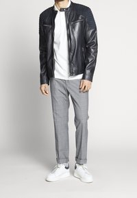 Czarna skórzana kurtka motocyklowa z pikowanymi akcentami na ramionach, biała koszulka polo, szare spodnie w kratę oraz białe trampki z granatowymi akcentami.