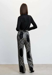 Black long-sleeve top paired with high-waisted black and white patterned wide-leg trousers featuring geometric lines and a smooth texture.
