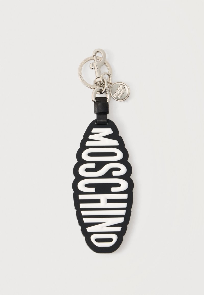 Μαύρο μπρελόκ με λευκή επιγραφή MOSCHINO με έντονα γράμματα, προσαρτημένο σε ασημί μεταλλικό κλιπ και στρογγυλή ετικέτα με σήμα.