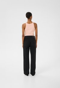 Zwarte wijde jeans gecombineerd met een lichtroze tanktop, die een gladde textuur en eenvoudig ontwerp toont, gezien vanaf de achterkant.