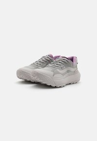 Zapatillas deportivas grises con una parte superior texturizada, cuello acolchado en lavanda, suela blanca gruesa y tacos prominentes para tracción.