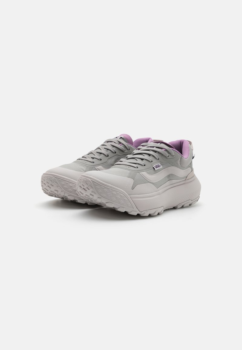 Zapatillas deportivas grises con una parte superior texturizada, cuello acolchado en lavanda, suela blanca gruesa y tacos prominentes para tracción.