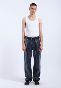 White sleeveless tank top, dark blue glossy oversized trousers, black belt, black sneakers, standing against a plain white background.