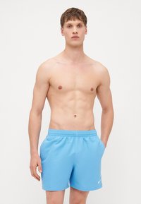 Shorts de bain bleu clair avec une taille élastique, des poches latérales et un petit logo Nike blanc sur la jambe gauche. Texture de tissu lisse.