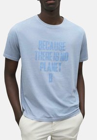 Camiseta de algodón de color azul claro con mangas cortas que presenta un eslogan impreso en azul más oscuro: "PORQUE NO HAY UN PLANETA B." Textura suave.
