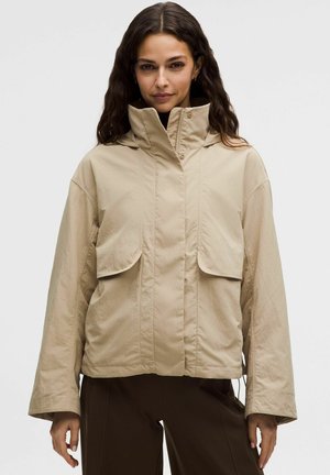 Beżowa lekka kurtka z wysokim kołnierzem, dwoma przednimi kieszeniami i luźnym krojem. Charakteryzuje się gładką fakturą i minimalistycznym designem.