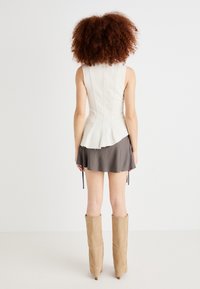 White, fitted corset top with vertical seams, paired with a gray mini skirt with ties. Knee-high beige boots complete the outfit.