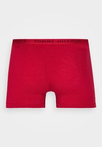 Punainen miesten bokserialushousut mustalla elastisella vyötärönauhalla, jossa on "Tommy Hilfiger" -brändäys.