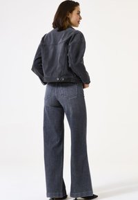 Donkerdenim jacket met een boxy pasvorm, voorzien van een kraag en knoopsluitingen. Gecombineerd met wijduitlopende, high-waisted donkerdenim jeans.