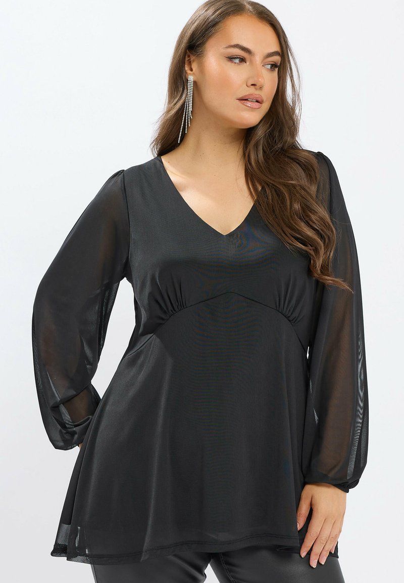 Tunique noire avec un col en V, des manches longues en translucide et un ourlet évasé. Présente une taille froncée et une texture lisse.