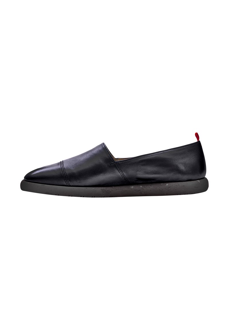 Scarpa nera in pelle slip-on con punta arrotondata, cuciture minime e un accento rosso a contrasto sul tallone, dotata di una suola nera testurizzata.