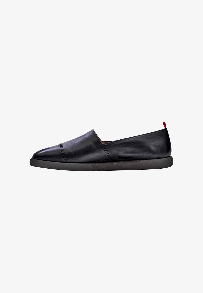 Scarpa nera in pelle slip-on con punta arrotondata, cuciture minime e un accento rosso a contrasto sul tallone, dotata di una suola nera testurizzata.