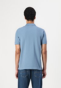 Svetlo modra polo majica s kratkim ovratnikom, kratkimi rokavi in gladko teksturo, v kombinaciji z modrimi jeans hlačami.