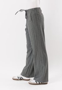Pantaloni a gamba larga a righe grigie con vita con coulisse, dotati di tasche frontali e realizzati in un tessuto morbido e testurizzato. Abbinati a sneaker bianche.