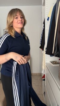 Námořnická modrá polo košile s bílými pruhy a plisovanou sukní s proužky, která je držena. Minimalistické pozadí s šatníkem a různými kusy oblečení.