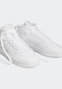 Ein Paar weiße Adidas-Leder-High-Top-Sneaker mit Schnürsenkeln, perforiertem Zehenbereich und Markenlogos auf der Zunge vor einem schlichten hellen Hintergrund.