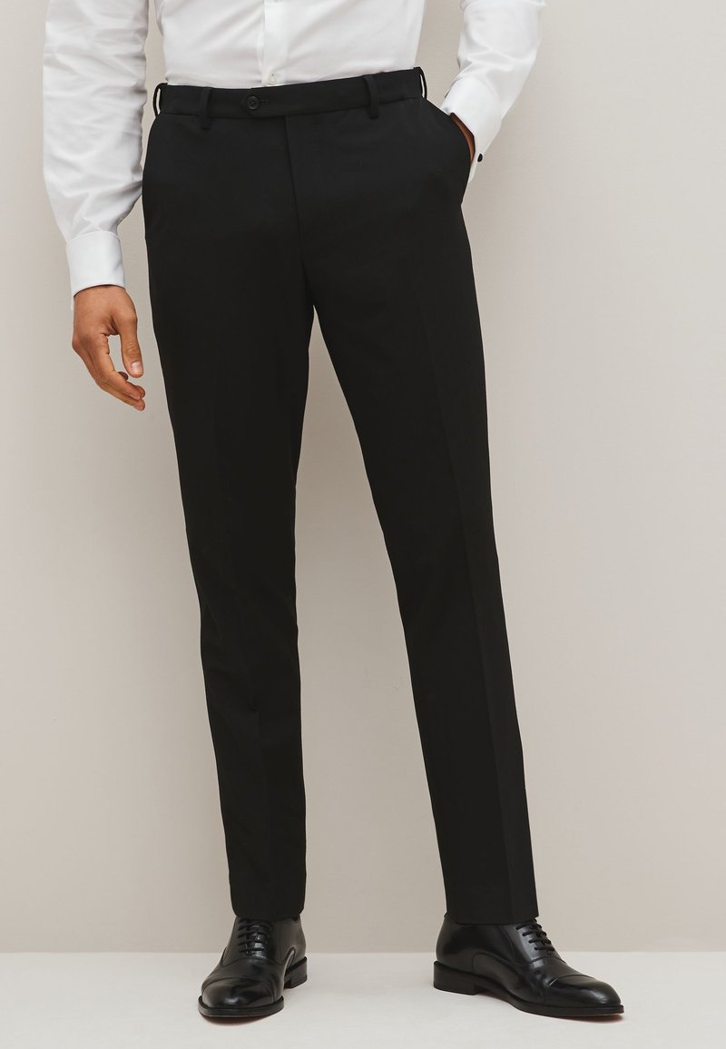 Zwarte op maat gemaakte broek van gladde stof, met een slim fit, rechte pijpen en een knoopsluiting, gecombineerd met zwarte leren schoenen.