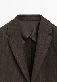 Brauner Woll-Blazer mit feinem Streifenmuster, mit Reverskragen und glatter Innenauskleidung, das sein maßgeschneidertes Design und seine Textur unterstreicht.
