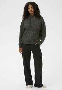 Donkergrijze gebreide hoodie met een buidelzak en trekkoordcapuchon, gecombineerd met zwarte wijde broek en lichtgekleurde schoenen.